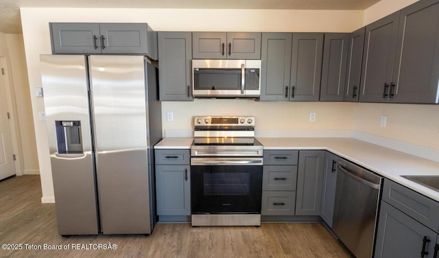 kitchen with appliances with stainless steel finishes, light countertops, light wood finished floors, and gray cabinetry