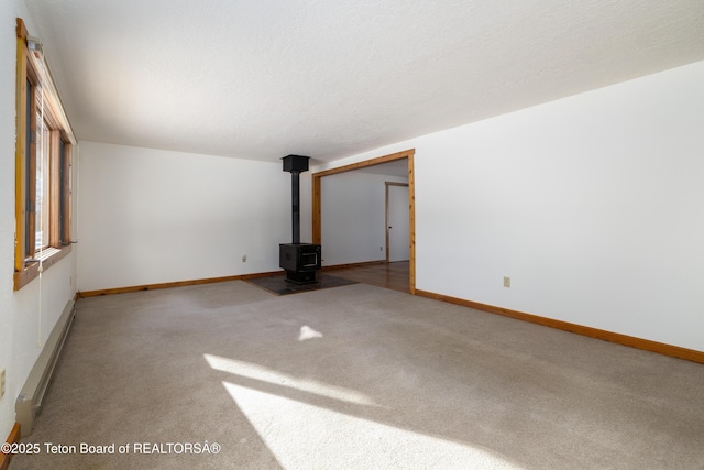 carpeted empty room featuring a wood stove and baseboard heating