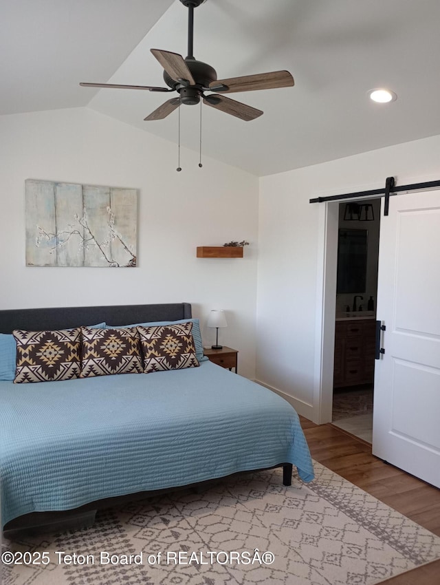 bedroom with ensuite bath, ceiling fan, wood-type flooring, a barn door, and lofted ceiling