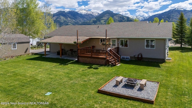 rear view of property featuring a deck with mountain view, a yard, a patio, and an outdoor fire pit