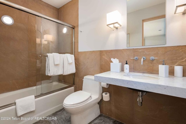 full bathroom with sink, combined bath / shower with glass door, toilet, decorative backsplash, and tile walls