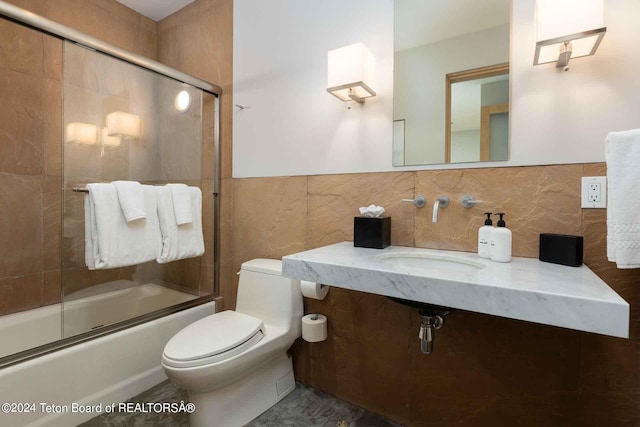 full bathroom with shower / bath combination with glass door, backsplash, sink, toilet, and tile walls