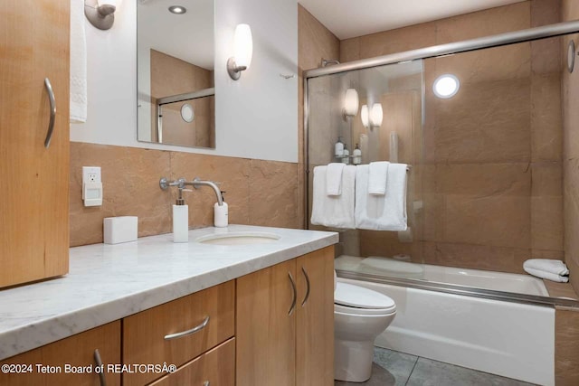 full bathroom featuring vanity, shower / bath combination with glass door, tile patterned floors, toilet, and tile walls