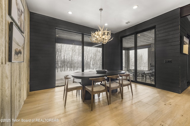 dining room featuring wood walls, a healthy amount of sunlight, and an inviting chandelier