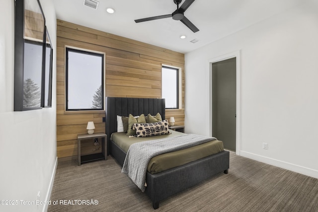 bedroom featuring wooden walls, ceiling fan, and dark colored carpet