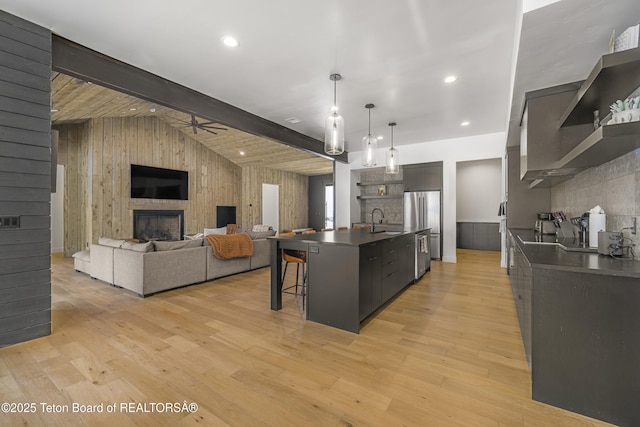 kitchen with light wood-type flooring, ceiling fan, sink, a fireplace, and an island with sink