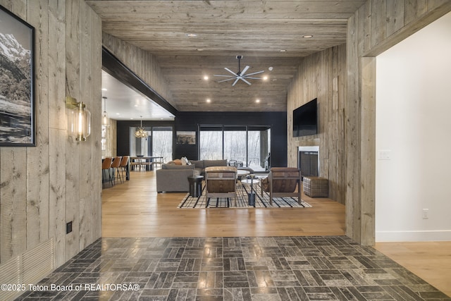 living room with wooden ceiling, high vaulted ceiling, wooden walls, ceiling fan, and a large fireplace