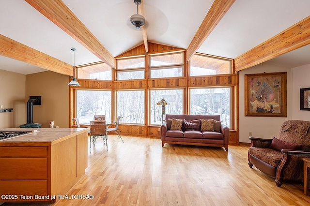 living room with ceiling fan, light wood-style flooring, and vaulted ceiling with beams