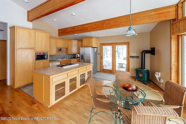kitchen featuring tile counters, a wood stove, black microwave, and light brown cabinetry