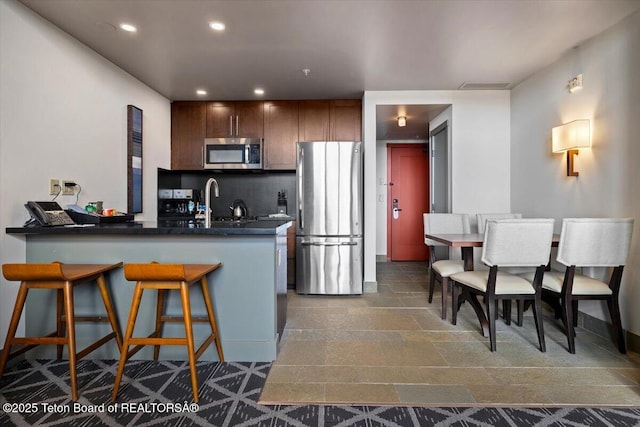 kitchen with kitchen peninsula, sink, a breakfast bar, decorative backsplash, and stainless steel appliances