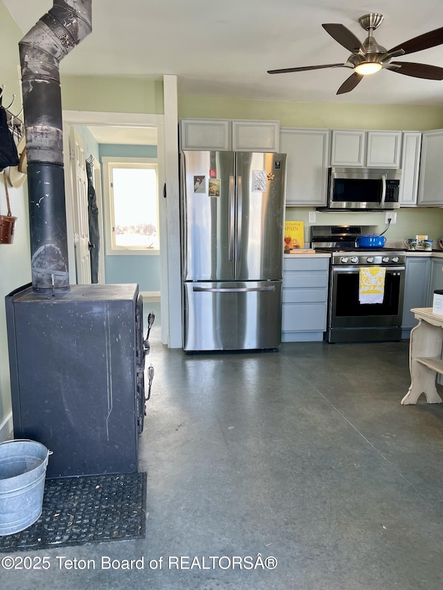 kitchen featuring a wood stove, finished concrete flooring, appliances with stainless steel finishes, and ceiling fan