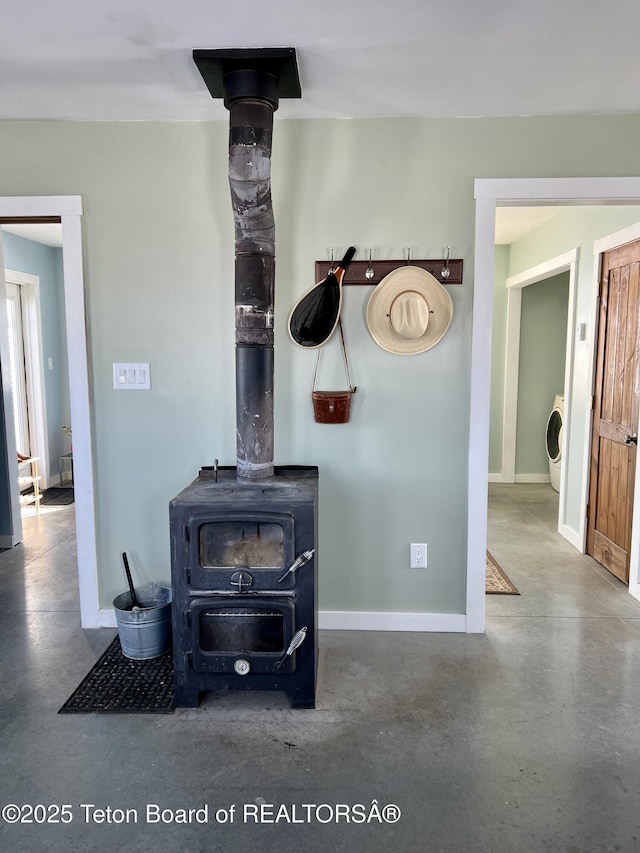 interior details with baseboards, washer / clothes dryer, finished concrete floors, and a wood stove