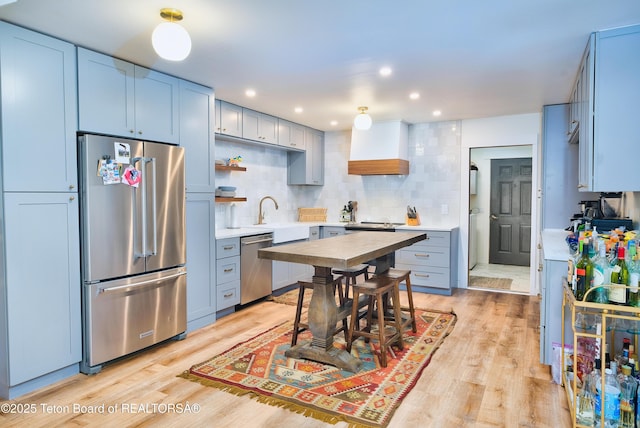 kitchen featuring backsplash, custom exhaust hood, sink, light wood-type flooring, and appliances with stainless steel finishes