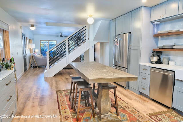 kitchen featuring stainless steel appliances, light hardwood / wood-style floors, decorative backsplash, ceiling fan, and gray cabinetry