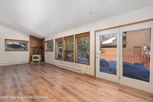 unfurnished living room with lofted ceiling, baseboard heating, plenty of natural light, and a wood stove