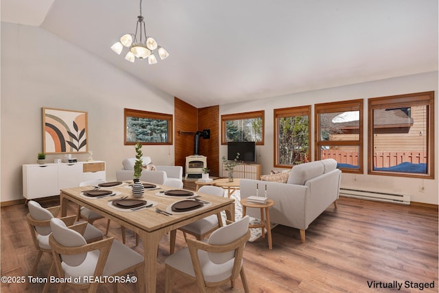 dining room featuring lofted ceiling, a chandelier, a baseboard radiator, light wood finished floors, and a wood stove