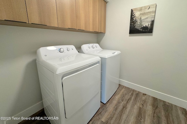 clothes washing area featuring hardwood / wood-style flooring, cabinets, and washer and clothes dryer