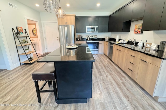 kitchen featuring appliances with stainless steel finishes, hanging light fixtures, a kitchen island, and light brown cabinets