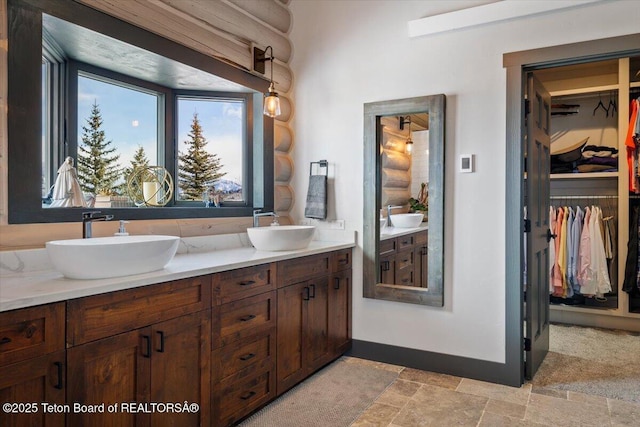 full bathroom with double vanity, rustic walls, stone finish floor, and a sink