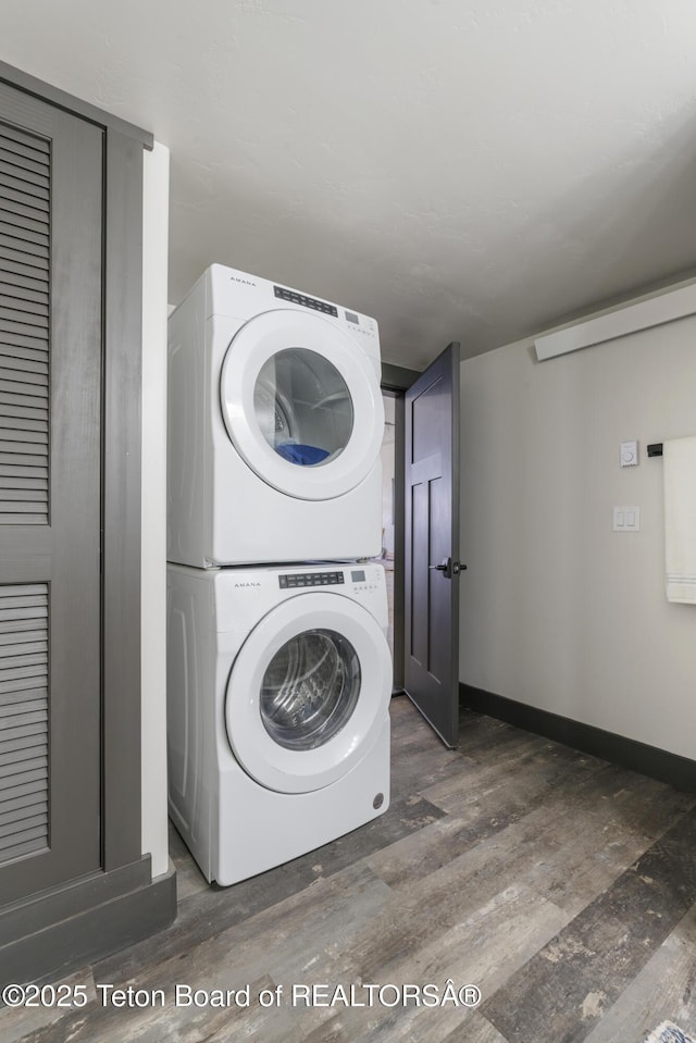 washroom featuring stacked washer and dryer, laundry area, baseboards, and wood finished floors