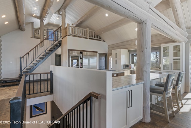 interior space featuring high vaulted ceiling, built in fridge, a breakfast bar, white cabinets, and beamed ceiling