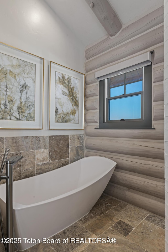 full bath with stone finish floor, a freestanding tub, log walls, and beamed ceiling