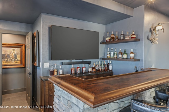 bar with light wood-style floors, indoor wet bar, and baseboards