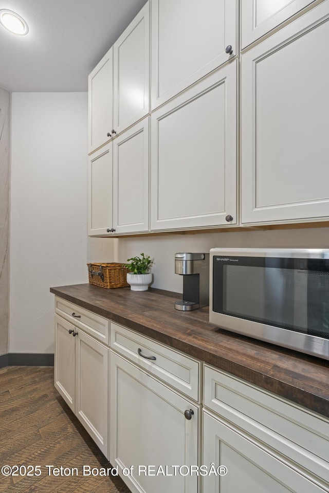 bar featuring dark wood-style floors, stainless steel microwave, and baseboards