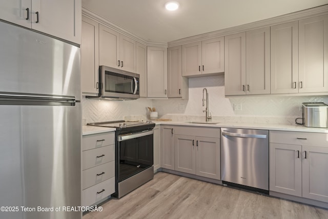 kitchen with light wood-type flooring, appliances with stainless steel finishes, gray cabinets, and a sink