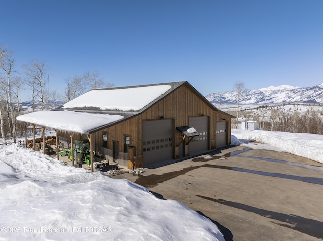 snow covered property with a detached garage, a mountain view, and an outbuilding