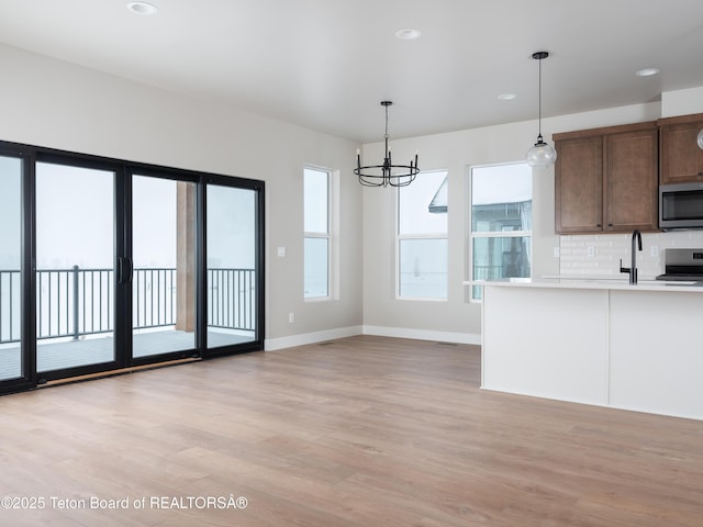 kitchen with light hardwood / wood-style floors, pendant lighting, decorative backsplash, an inviting chandelier, and appliances with stainless steel finishes