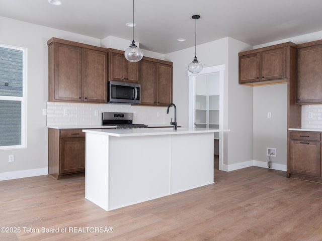 kitchen with backsplash, a center island with sink, pendant lighting, light wood-type flooring, and stainless steel appliances