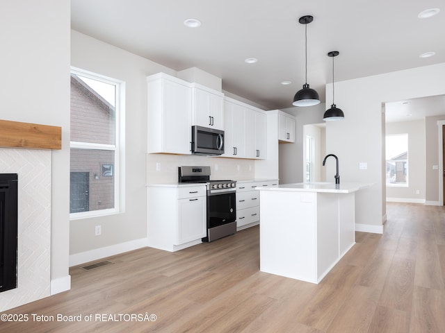 kitchen featuring appliances with stainless steel finishes, white cabinets, hanging light fixtures, and an island with sink