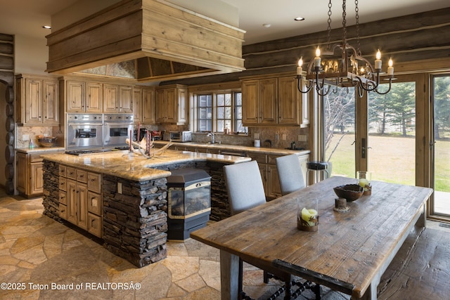 kitchen featuring light stone countertops, an island with sink, an inviting chandelier, sink, and tasteful backsplash