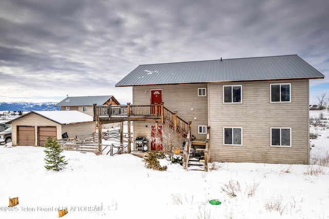 snow covered back of property with a garage, an outdoor structure, and a deck