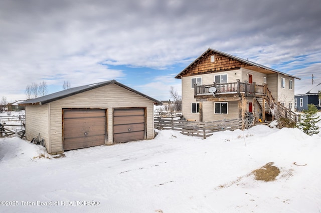 snow covered rear of property with a garage and a balcony