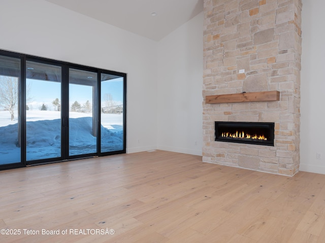 unfurnished living room with a fireplace, high vaulted ceiling, and light wood-type flooring