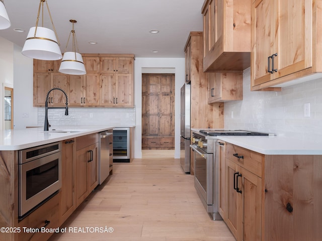 kitchen with wine cooler, sink, hanging light fixtures, appliances with stainless steel finishes, and light hardwood / wood-style floors