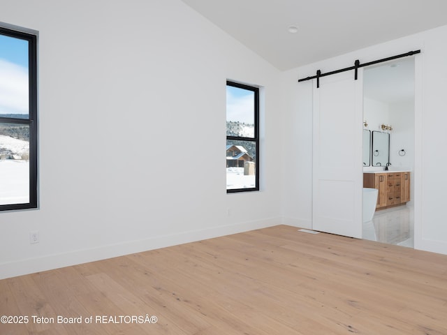 unfurnished room featuring a barn door, hardwood / wood-style floors, and lofted ceiling