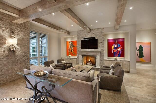 cinema room featuring beamed ceiling, a stone fireplace, and light wood-type flooring