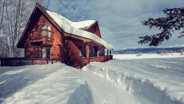 snow covered property featuring a balcony and a mountain view