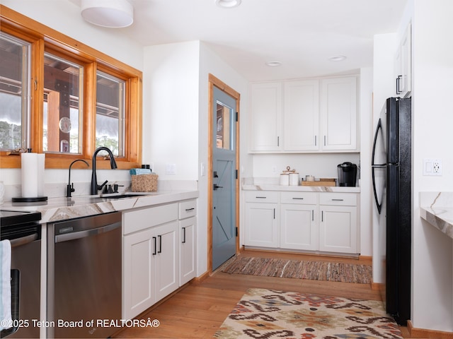 kitchen featuring sink, white cabinetry, light hardwood / wood-style flooring, stainless steel appliances, and light stone countertops