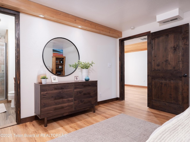 bedroom featuring beamed ceiling, ensuite bath, and light hardwood / wood-style flooring