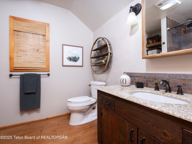 bathroom featuring tasteful backsplash, wood-type flooring, lofted ceiling, vanity, and toilet