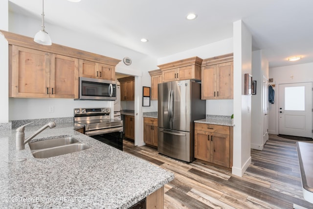 kitchen with light stone counters, stainless steel appliances, sink, and hanging light fixtures