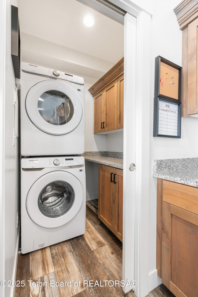 laundry area featuring cabinets, stacked washer and dryer, and dark hardwood / wood-style flooring