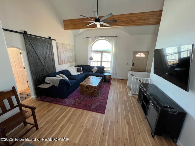 living room with ceiling fan, a barn door, high vaulted ceiling, and light hardwood / wood-style floors