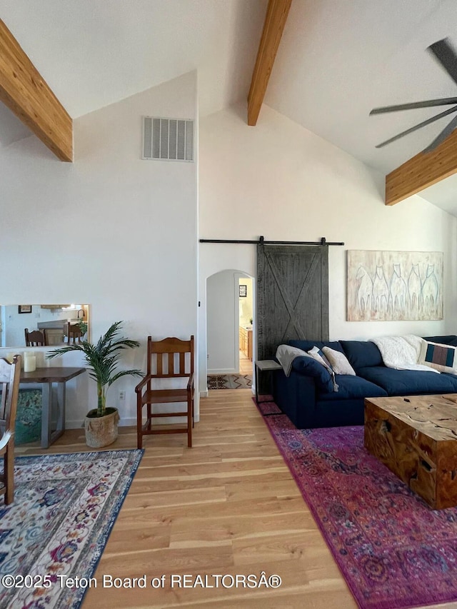 living room featuring wood-type flooring, high vaulted ceiling, beamed ceiling, ceiling fan, and a barn door