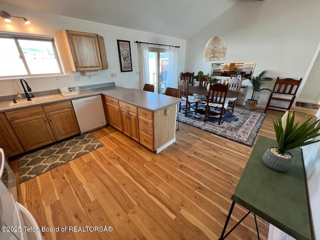 kitchen with sink, hanging light fixtures, white dishwasher, kitchen peninsula, and light hardwood / wood-style flooring