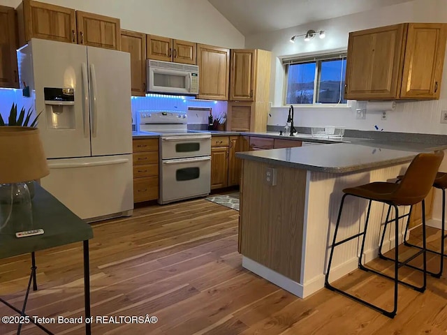 kitchen featuring tasteful backsplash, vaulted ceiling, a kitchen breakfast bar, white appliances, and hardwood / wood-style floors